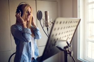 Young smiling woman in with headphones singing in recording studio.